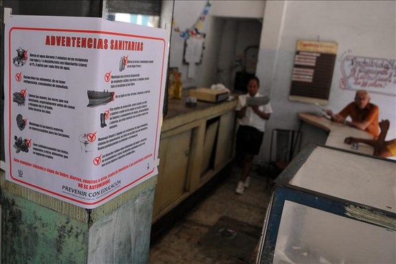 Varias personas conversan en una cafetería, donde se puede ver un cartel alusivo al control sanitario en la capital cubana. EFE/Archivo