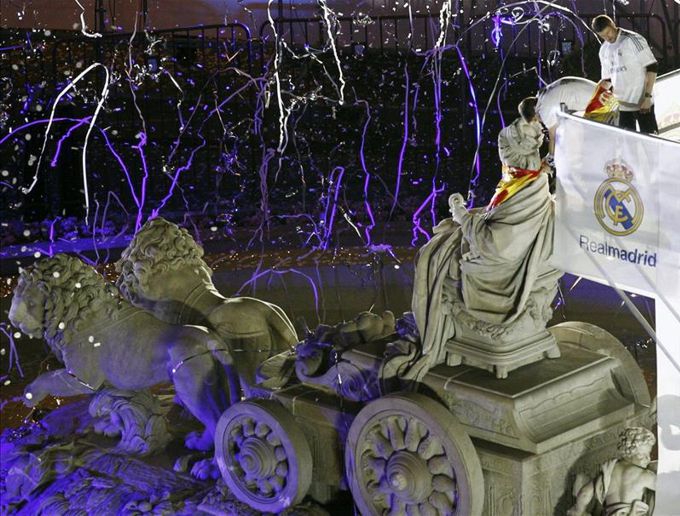 El capitán del Real Madrid, Iker Casillas, coloca una bandera española y una bufanda con el escudo del equipo en torno al cuello de la diosa Cibeles. EFE