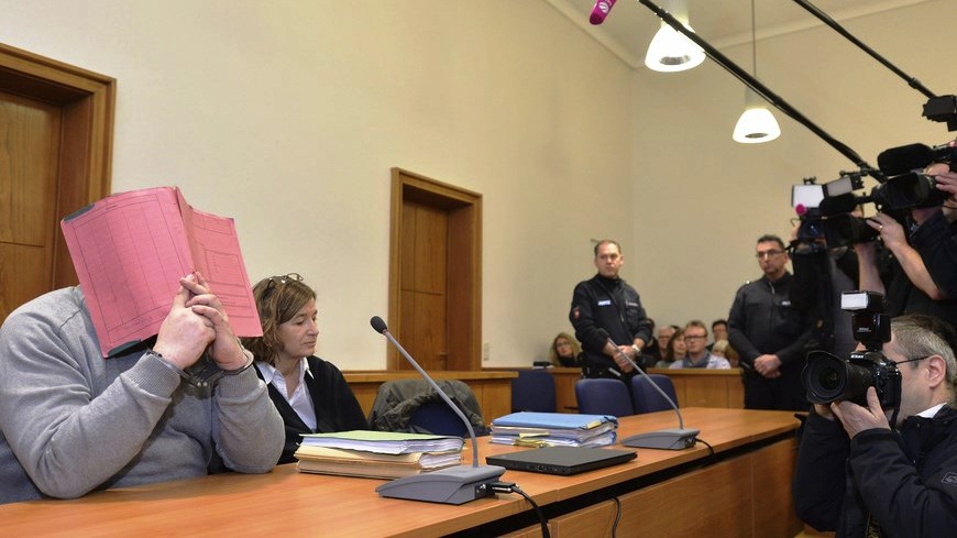 El exenfermero Niels H. (izq) se cubre el rosto mientras permanece en el banquillo de los acusados en el tribunal de distrito de Olenburg (Alemania