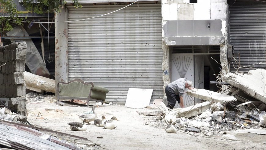 Un hombre busca entre los escombros junto a la entrada de un edificio en el campo de refugiados de Al Yarmuk, en el sur de Damasco (Siria). EFE/Archivo