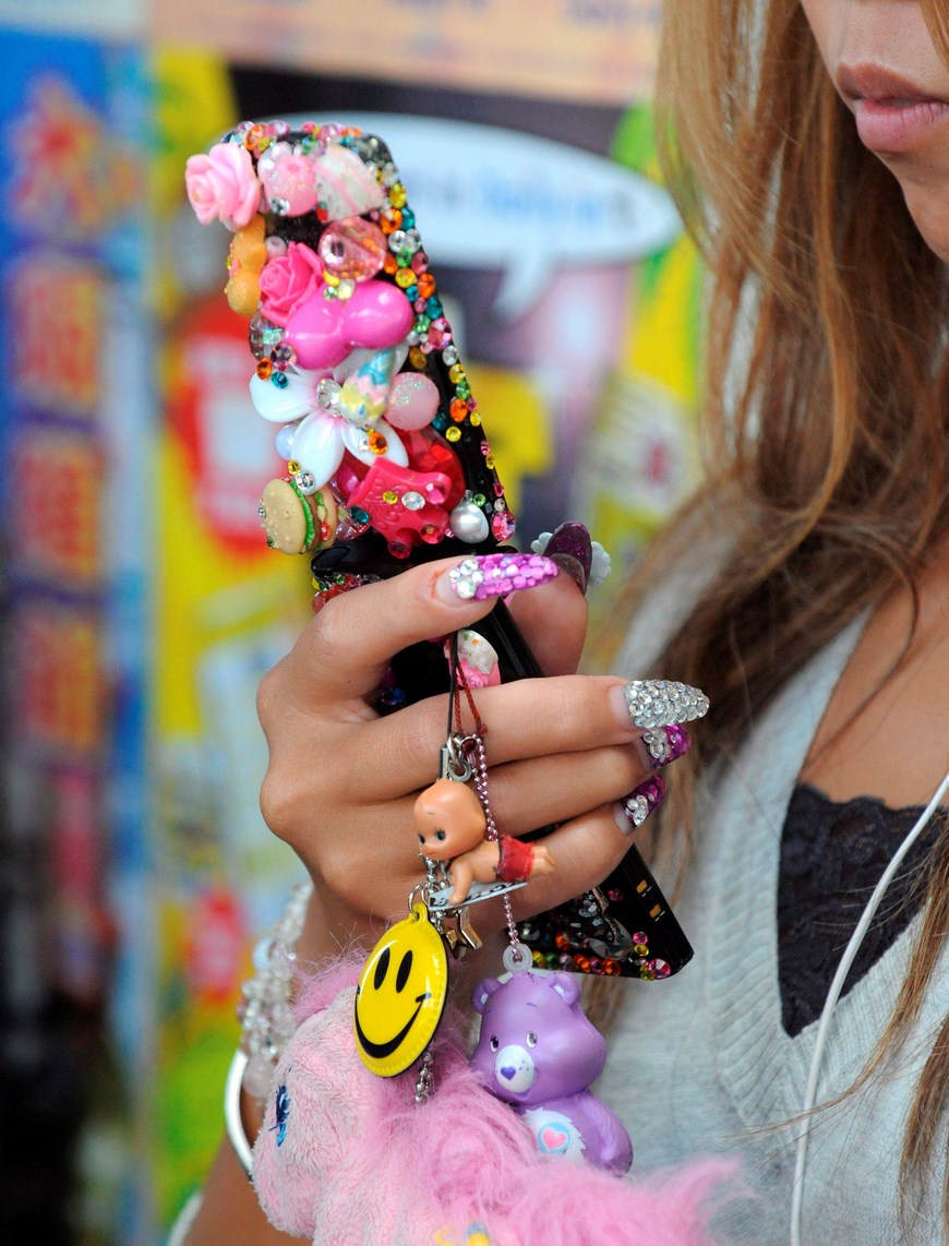 Una joven usa su teléfono móvil, completamente cubierto con pegatinas y otros tipos de ornamentos, en una estación de Osaka (Japón). EFE/Archivo