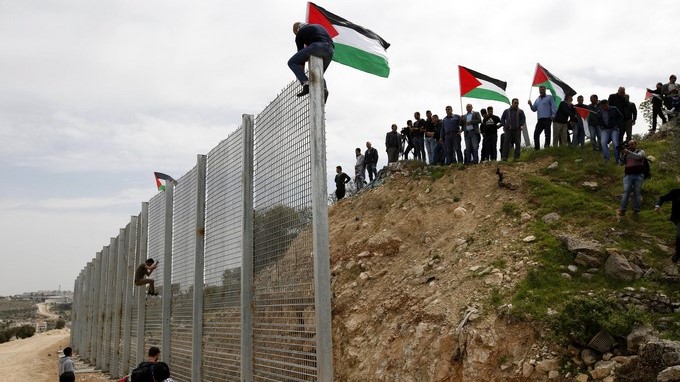 Ciudadanos palestinos colocan su bandera en el muro israelí durante una protesta en el Día Nacional de la Tierra. EFE/Archivo