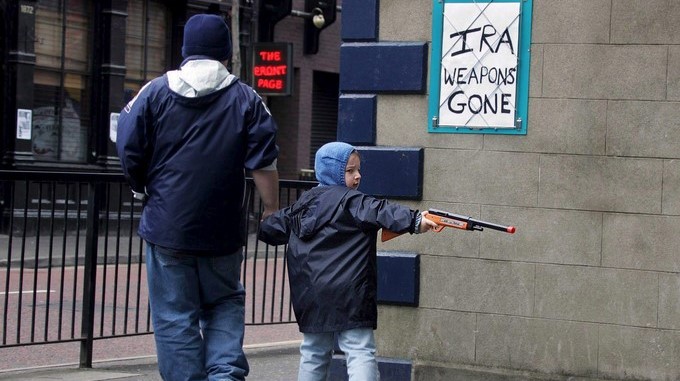 Un niño pasa frente a un tablón de edictos en el centro de Belfast, Irlanda del Norte, delante de un cartel alusivo al desarme del IRA. EFE/Archivo