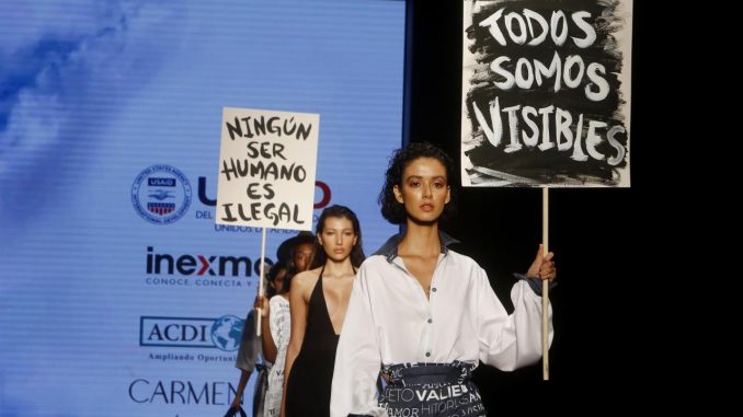 Varias modelos desfilan diseños de la diseñadora venezolana Carmen Nava mientras sostienen unos carteles con frases como "Todos somos visibles" y "Ningún ser humano es ilegal", durante la pasarela "Visibles", hoy, en Colombiatex + Colombiamoda 2021, en Medellín (Colombia). EFE/Luis Eduardo Noriega A. Colombiamoda