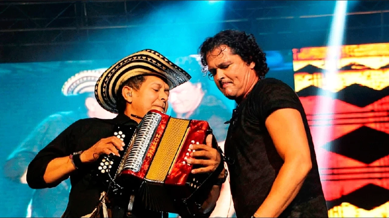 Egidio Cuadrado toca el acordeón junto a Carlos Vives en un escenario.