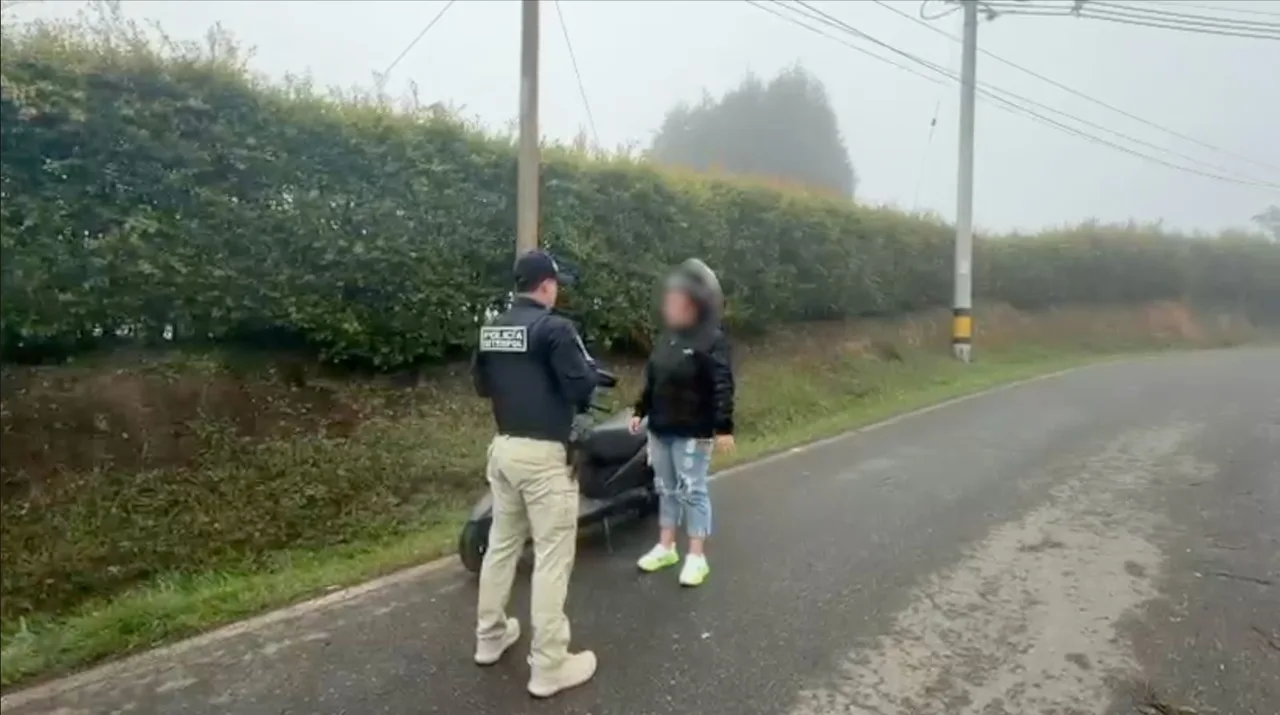 ¡Cayó en Medellín! Colombiana buscada por Suecia habría extorsionado con falsos correos de la Policía sueca 1 Uniformado de Interpol conversa con la mujer retenida junto a una motocicleta en una vía rural